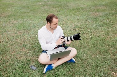 Dizüstü bilgisayar ve kamera kullanarak parkta genç adam fotoğrafçı