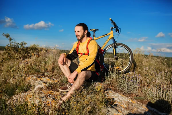 Hombre sentado bajo la luz del sol en el día cerca de su bicicleta — Foto de Stock