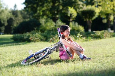 Onun Bisiklet yeşil çim üzerinde yakın oturan küçük kız.