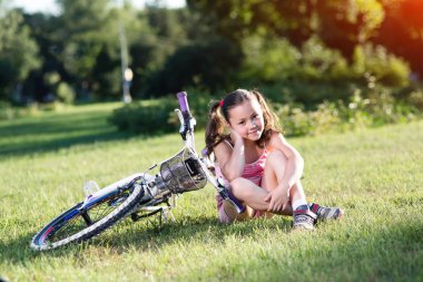 Onun Bisiklet yeşil çim üzerinde yakın oturan küçük kız.