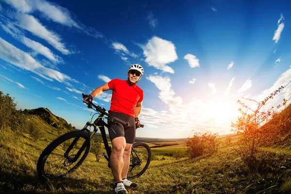 Ciclista de pé com mountain bike na trilha ao pôr do sol — Fotografia de Stock