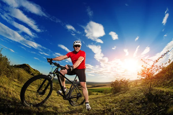 Ciclista de pé com mountain bike na trilha ao pôr do sol — Fotografia de Stock