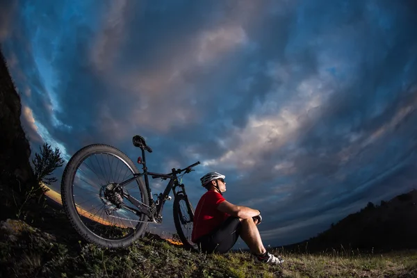 Парень отдыхает, сидя рядом со своим велосипедом — стоковое фото