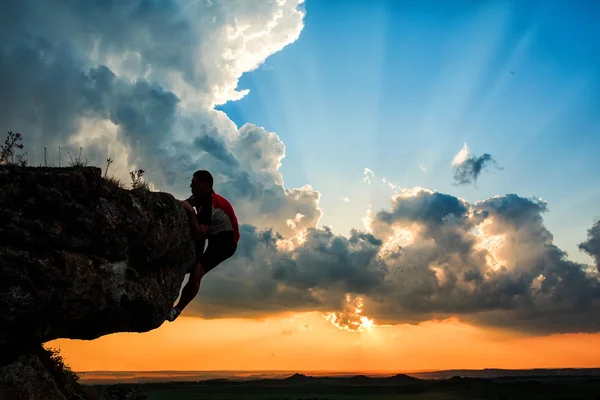 Un tipo se sienta en una roca mirando el atardecer — Foto de Stock