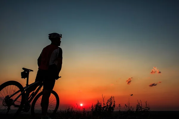 Silhueta de um motociclista e bicicleta no fundo do céu . — Fotografia de Stock