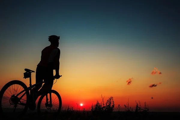 Silhueta de um motociclista e bicicleta no fundo do céu . — Fotografia de Stock