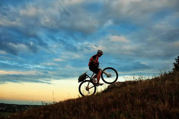 Silhueta de um motociclista e bicicleta no fundo do céu . — Fotografia de Stock