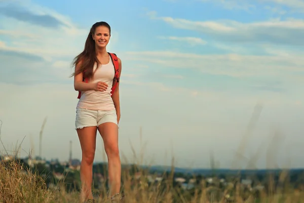 Mladá žena s červeným batohem, chůze na západ slunce v létě. — Stock fotografie