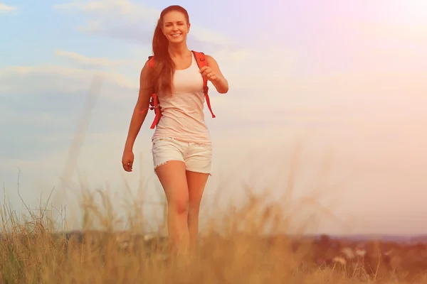 夏の日没の上を歩く赤いバックパックを持つ若い女性. — ストック写真