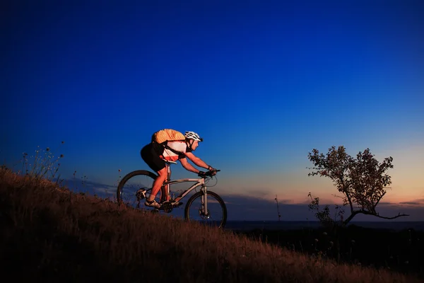 Silhueta de um motociclista e bicicleta no pôr do sol fundo . — Fotografia de Stock