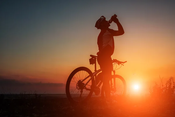 Silhueta de um motociclista e bicicleta no fundo do céu . — Fotografia de Stock