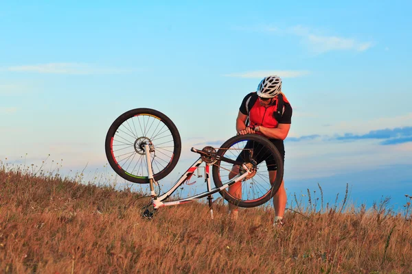 Hombre ciclista reparando una bicicleta contra el cielo azul — Foto de Stock