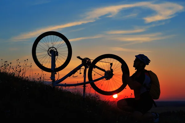 Silhouette of man cyclist repairing a bike  against sunset — Stock Photo, Image