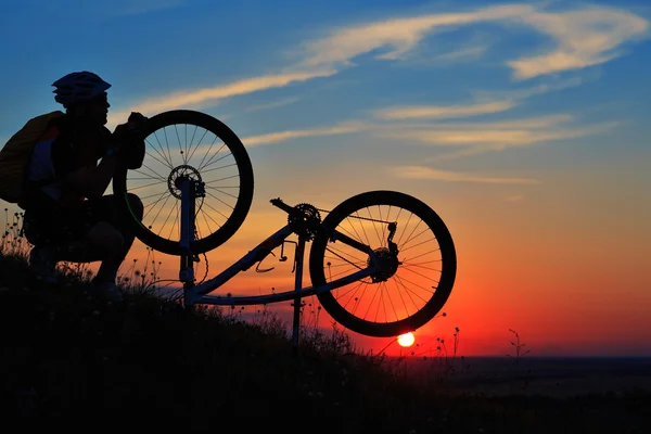 Sziluettjét férfi kerékpáros ellen sunset kerékpár javítás — Stock Fotó