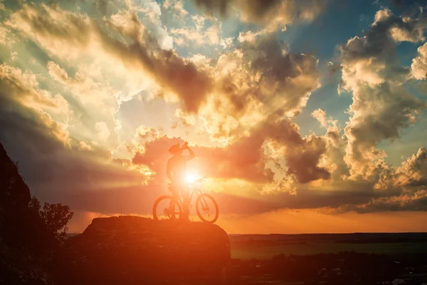 Silhueta de um motociclista e bicicleta no fundo do céu . — Fotografia de Stock