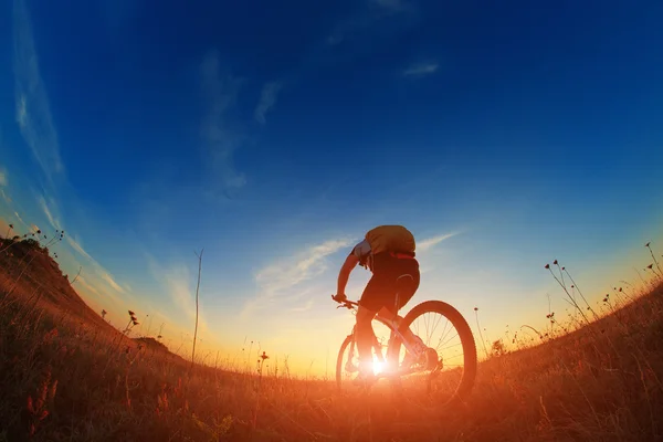 Silhueta de um motociclista e bicicleta no fundo do céu . — Fotografia de Stock