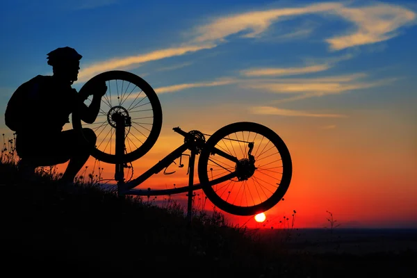 Homem ciclista reparar uma bicicleta contra o céu azul — Fotografia de Stock