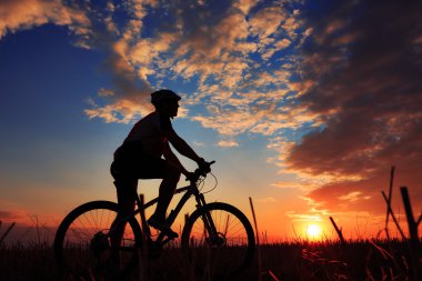 Silhouette bir motorcu ve gün batımı arka plan üzerinde bisiklet.