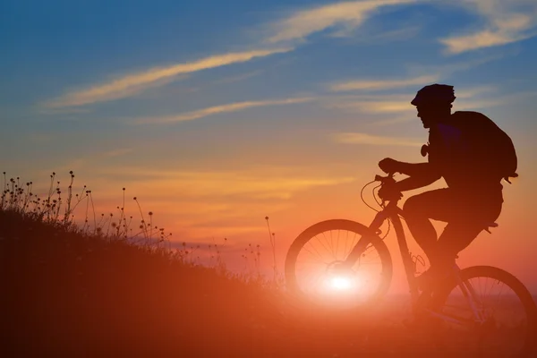 Silhueta de um motociclista e bicicleta no pôr do sol fundo . — Fotografia de Stock