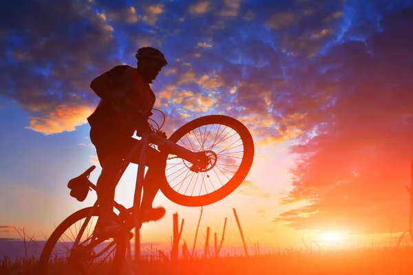 Silhueta de um motociclista e bicicleta no pôr do sol fundo . — Fotografia de Stock