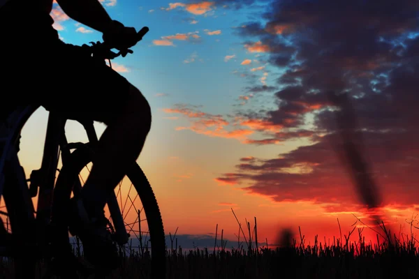 Silhouette d'un motard et vélo sur fond de coucher de soleil . — Photo