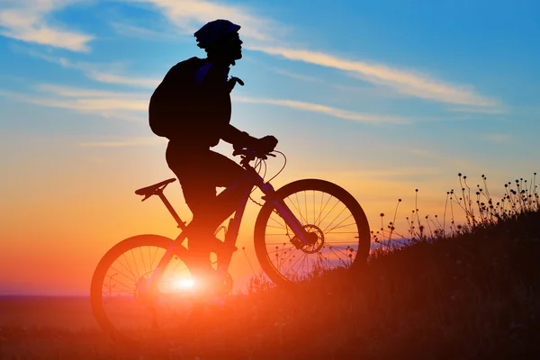 Silhueta de um motociclista e bicicleta no pôr do sol fundo . — Fotografia de Stock