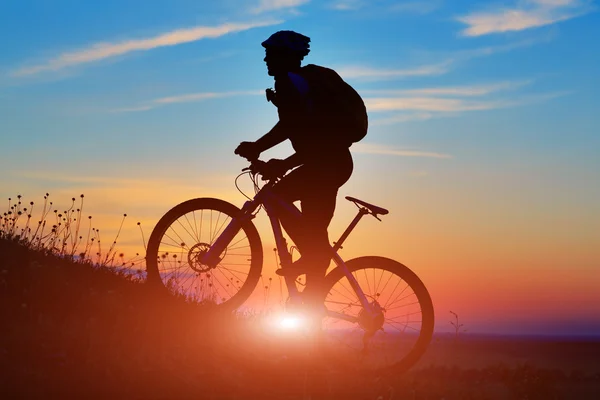 Silhueta de um motociclista e bicicleta no pôr do sol fundo . — Fotografia de Stock