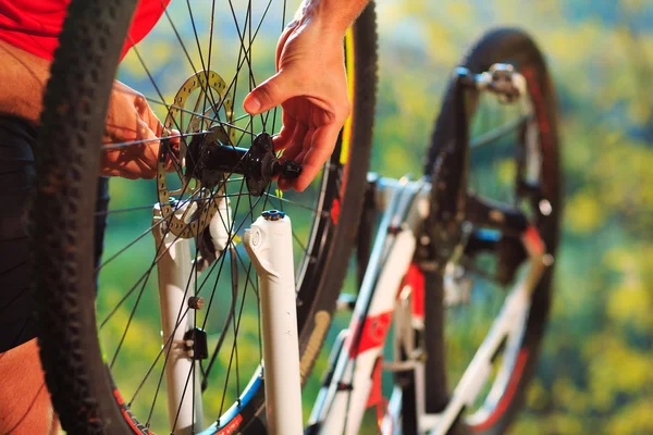 Homem ciclista reparar uma bicicleta contra o céu azul — Fotografia de Stock