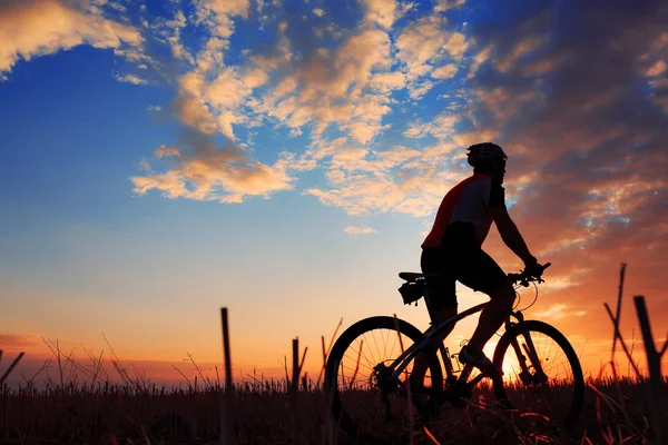 Silhueta de um motociclista e bicicleta no pôr do sol fundo . — Fotografia de Stock