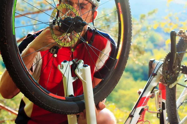 Uomo ciclista che ripara una bicicletta contro il cielo blu — Foto Stock