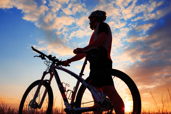 Silhouette di un motociclista e bicicletta sullo sfondo del tramonto . — Foto Stock