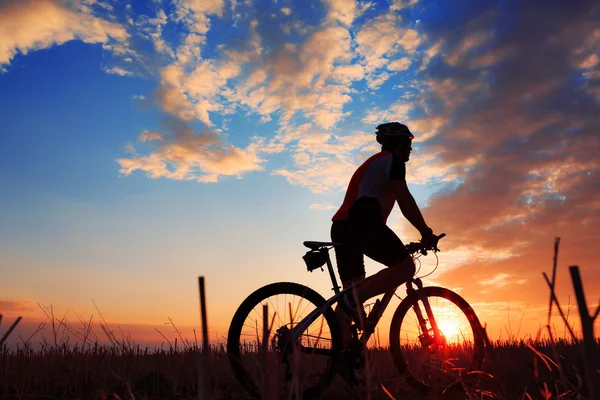 Silhouette di un motociclista e bicicletta sullo sfondo del tramonto . — Foto Stock