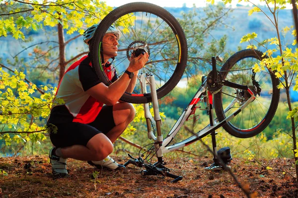Чоловік-велосипедист ремонтує велосипед проти блакитного неба — стокове фото