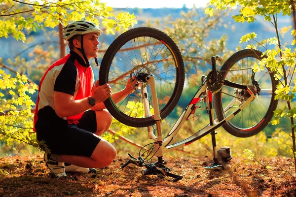 Uomo ciclista che ripara una bicicletta contro il cielo blu Fotografia Stock