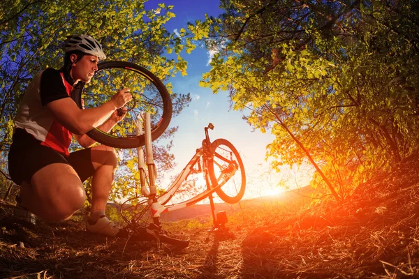 Man wielrenner herstellen een fiets tegen blauwe hemel — Stockfoto