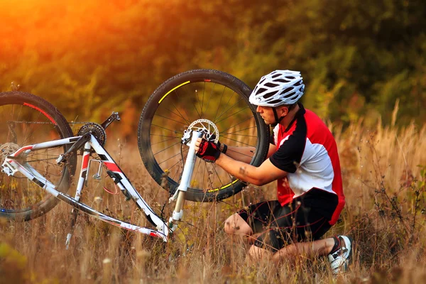 Joven reparando bicicleta de montaña en el bosque —  Fotos de Stock