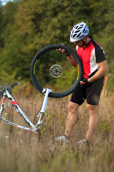 Joven reparando bicicleta de montaña en el bosque —  Fotos de Stock