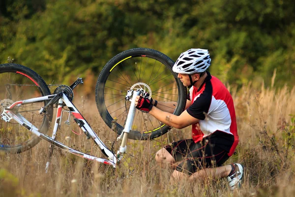 Jeune homme réparant le vélo de montagne dans la forêt — Photo