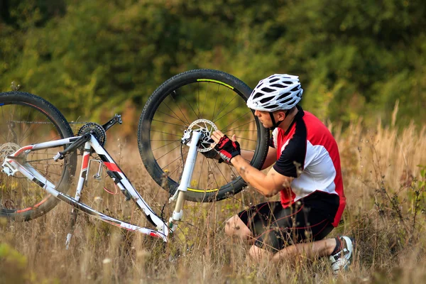 Hombre ciclista reparando una bicicleta contra la naturaleza verde —  Fotos de Stock