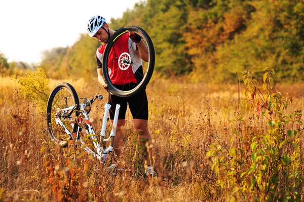 Людина-велосипедист ремонтує велосипед проти зеленої природи — стокове фото