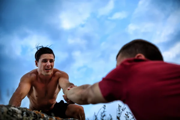 The rock climber gives hand for help to the partner