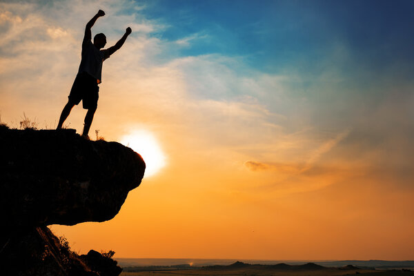 Человек стоит у креста на вершине горы
