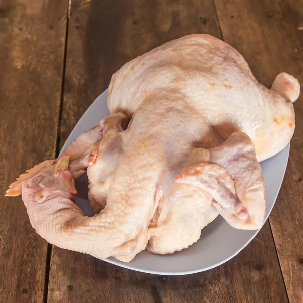 Ωμό κοτόπουλο σε ένα πιάτο σε ένα ξύλινο τραπέζι. — Φωτογραφία Αρχείου