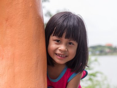 Küçük kız bir ağacın arkasından dışarı bakıyor.