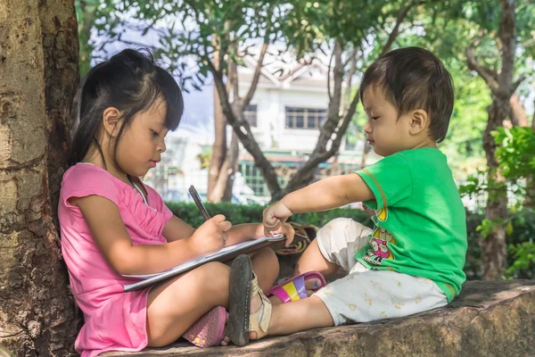 Outdoor portrait of a cute little girl and boy writing a book — Stock Photo, Image