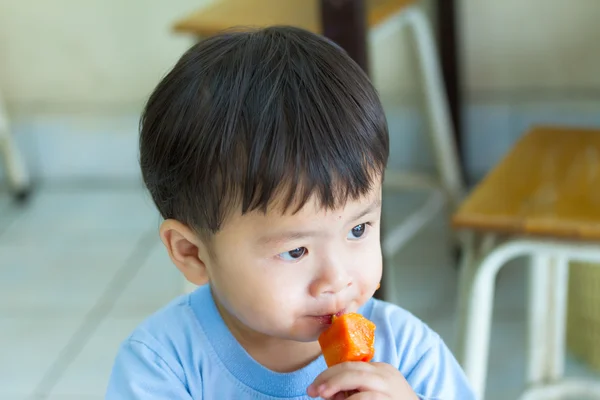 Portrait asian boy eating papaya on wood tip. — Stock Photo, Image