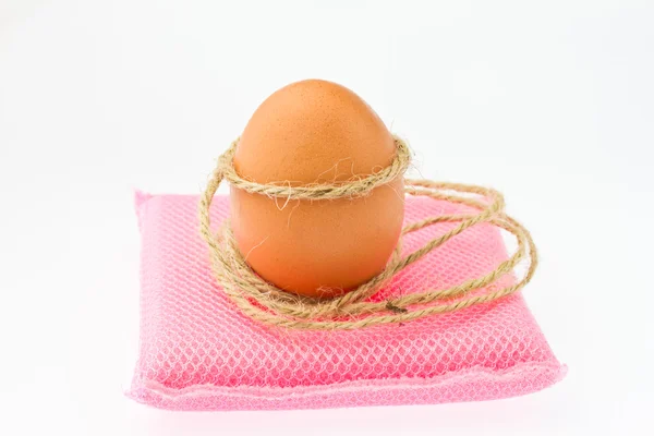 Huevo marrón atado por cuerda sobre esponja rosa y fondo blanco — Foto de Stock