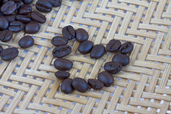 Semillas de café corazón sobre fondo de bambú de madera —  Fotos de Stock