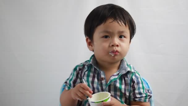 Junge isst Joghurt auf weißem Hintergrund — Stockvideo