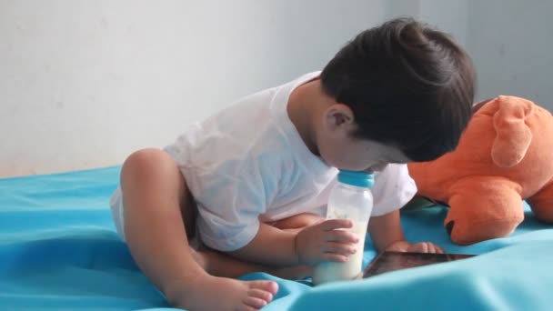 Kleiner Junge trinkt Milch aus Flasche auf dem Bett — Stockvideo